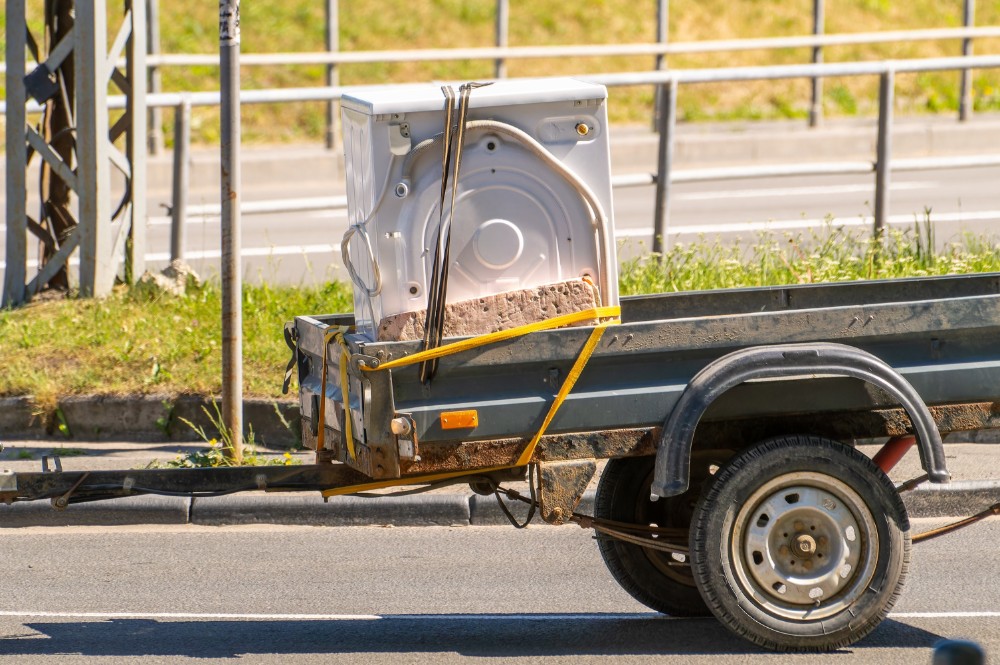 Old washing machine strapped to a small utility trailer for appliance junk removal and recycling